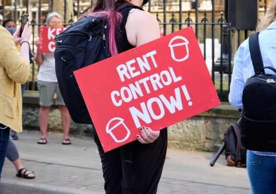 protester holding a rent control now sign at a housing crisis rally