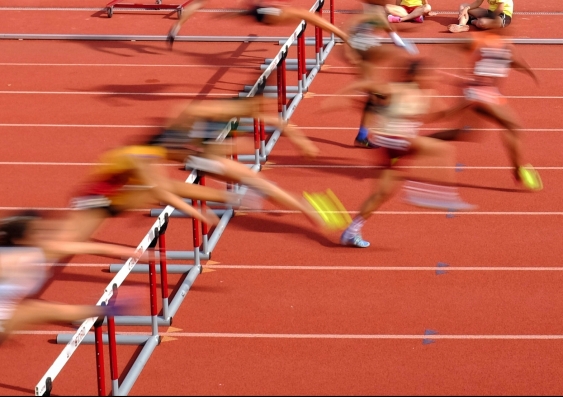 Runners on an athletics track jumping hurdles