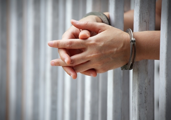 A pair of handcuffed hands clasped around some prison bars