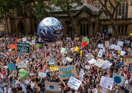 Crowds of people with signs and a globe of the world gather before a building to protest against climate change