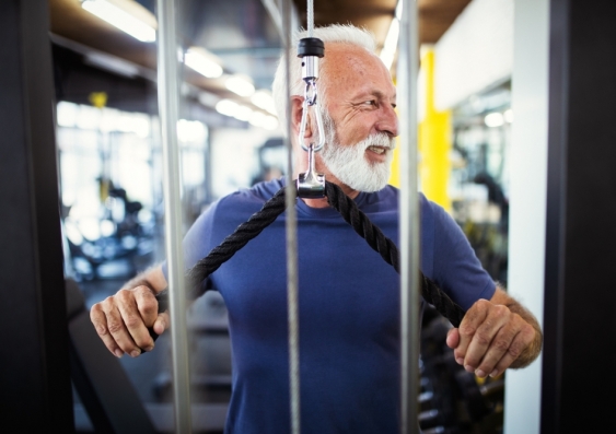 Smiling older man using weight machine at the gym