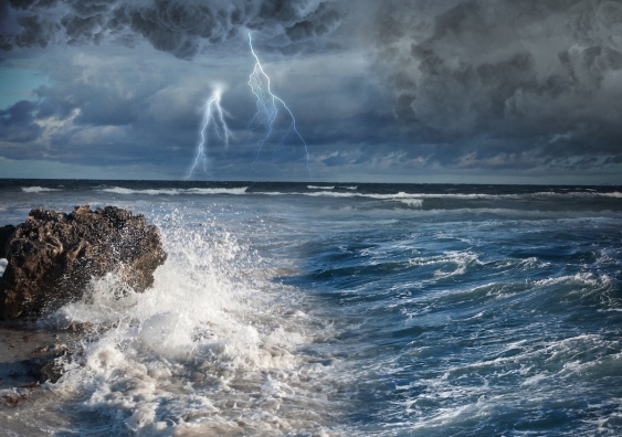Lightning over the ocean and waves crashing on rocks
