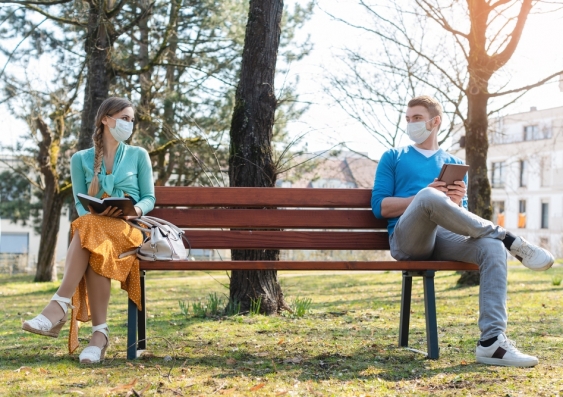 Two people sitting on a bench, social distancing and wearing masks