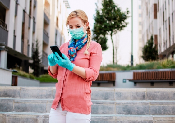 A woman wearing a protective mask and gloves uses a mobile phone
