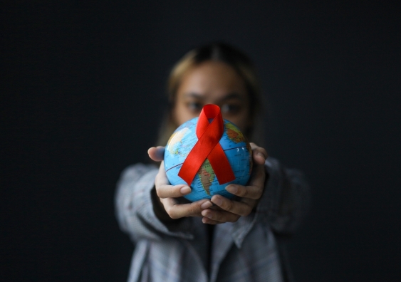 person holding a globe with a red ribbon attached to it - the universal symbol of awareness and support for people living with HIV. 