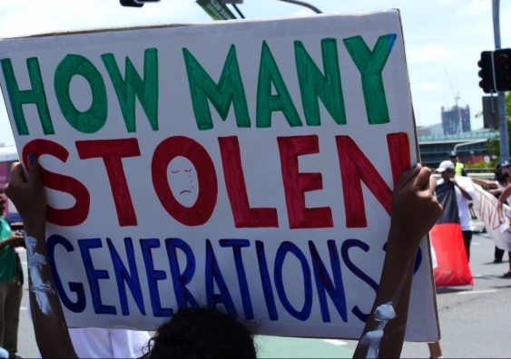 Man at protest holding sign that says how many stolen generations