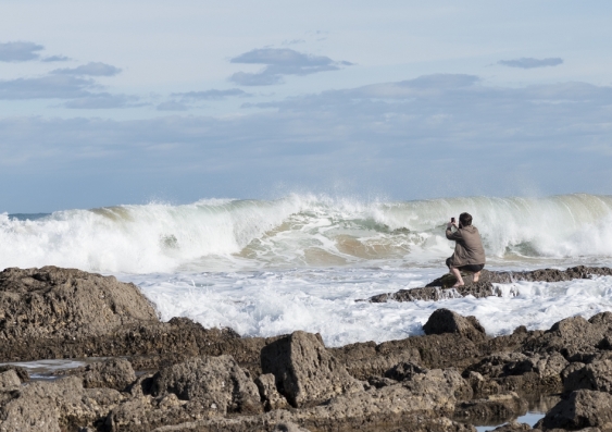 Man taking photos of waves on rocks