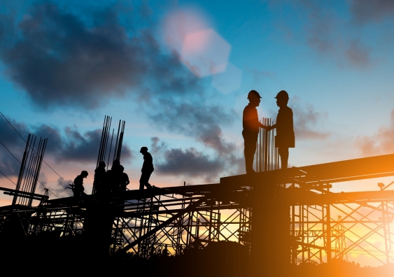 Silhouettes of two construction workers shaking hands on a construction site