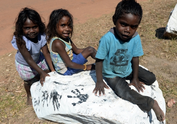 three indigenous children sitting on a rock and smiling