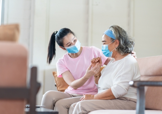 Two women wearing medical facemasks, one providing support as the other struggles with respiratory discomfort