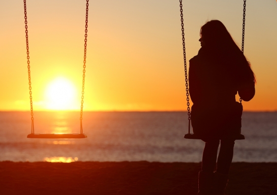 woman alone on a swing set looking at a sunset