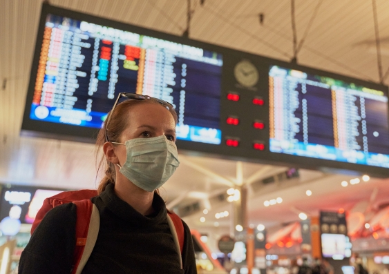 woman in mask in front of airport flight advisory board