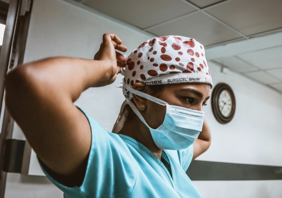 Woman in scrubs wearing surgical cap puts on a surgical face mask