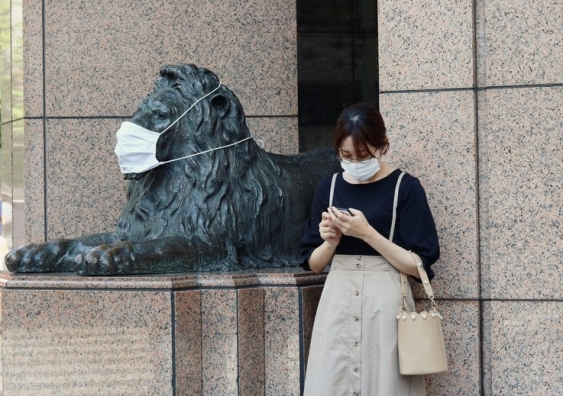 Woman stands next to a lion statue, both wearing face masks