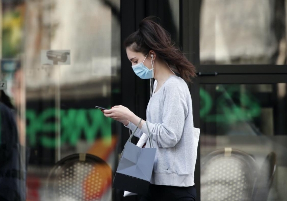 Woman wearing face mask using phone as she walks down the street