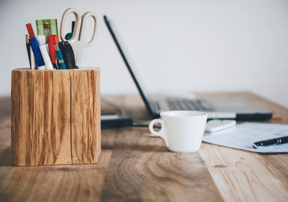 Wooden stationery caddy, white coffee mug and laptop on a wooden desk