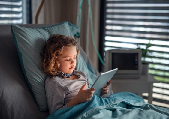 Young girl in hospital bed using an electronic tablet