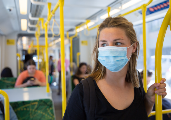 A young woman wearing a face mask riding public transport
