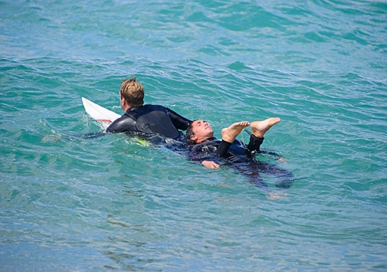 A surfer in wetsuit tows a person on the back of his board
