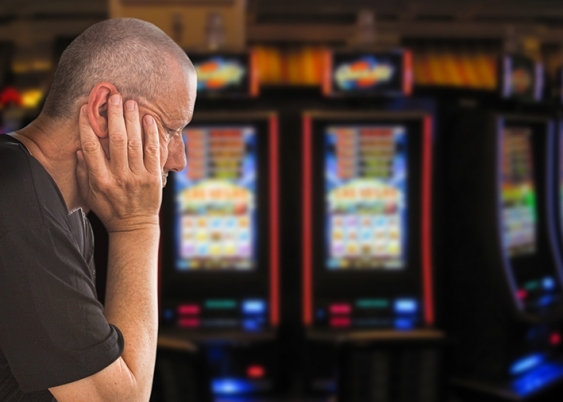 A man looking forlorn with his head cradled in his hand with pokies in the background