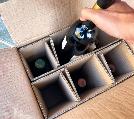 a hand taking a wine bottle out of cardboard box