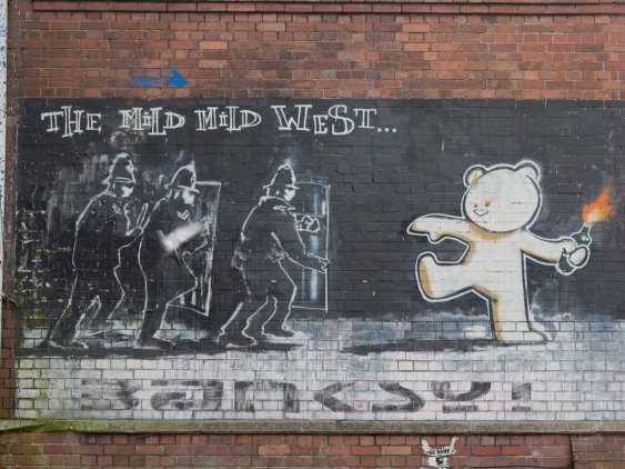 A graffiti of Banksy called The Mild Mild West, of a bear with fire in his hand aiming at three police officers.