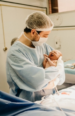 Man in hospital scrubs cradles newborn baby