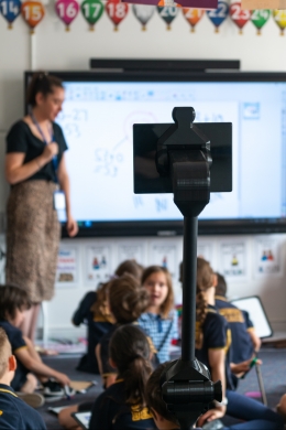 Telepresence robot surrounded by other students as teacher gives lesson
