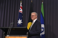 Anthony Albanese standing in front of the Australian, Aboriginal and Torres Strait Islander flags