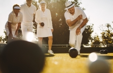 elderly man playing bowls in a lawn with his friends