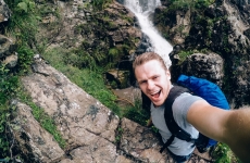 person taking selfie on rocks close to waterfall