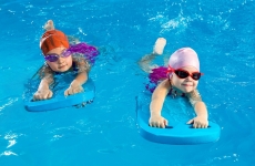 Two children with caps and goggles use kickboards in a swimming pool