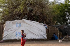 Small child in front of a UNHCR branded tent in a refugee camp