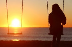 woman alone on a swing set looking at a sunset