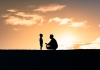 A child and adult face each other in silhouette at sunset