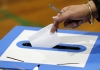 Close-up of a hand dropping in a folded piece of voting paper into a ballot box