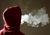 A hooded figure breathes out vape smoke