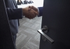 Close up of two people shanking hands behind a door slightly ajar