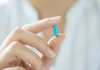 A blue capsule is held between thumb and forefinger