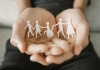 pair of hands with paper cut-out of people holding hands, including one in wheelchair