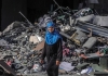 a palestinian women walks past the rubble of a building