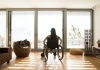 a woman in a wheelchair sits looking at a window filled with bright light