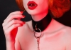 a woman wearing a leather collar and red lipstick holds a red cherry to her lips