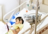 An ill child lies in a hospital bed attached to a medical device