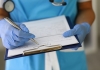 Close up of a person in hospital scrubbs making notes on a clipboard