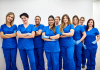 9 nurses who are all women stand in a row in their scrubs