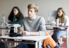 Photo of teenage boy sitting in classroom with two female classmates in background