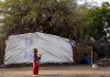 Small child in front of a UNHCR branded tent in a refugee camp