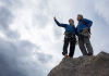 Two people stand on a rock taking a selfie with a cloudy sky behind