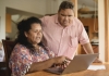 Aboriginal couple in their 50s at home using the internet, man leaning over woman and looking at screen